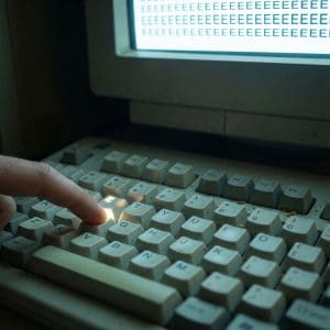 빛나는 화면에 같은 글자가 여러 개 찍힌 채, 가까이서 본 컴퓨터 키보드의 한 키가 눌려 있습니다.